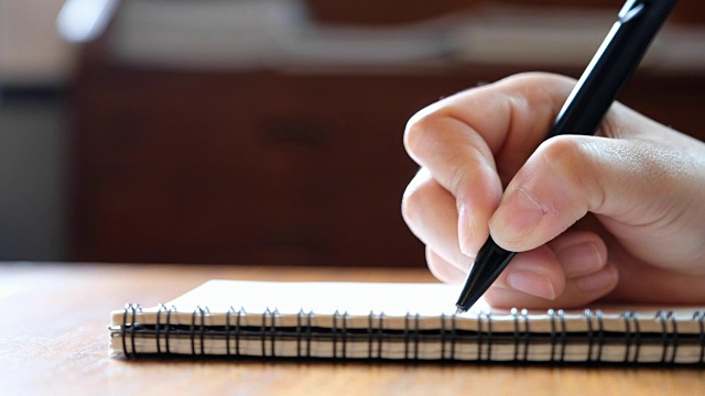一个女人的手写在木桌上的空白笔记本上视频素材