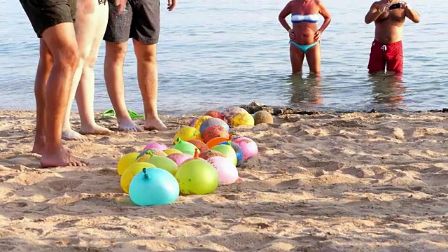 在海滩上，在沙滩上是装满水而不是空气的气球。人们在海滩上休息玩游戏视频下载