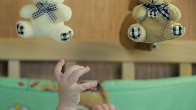 一个躺在婴儿床上的5个月大的男孩的小手想去够儿童旋转木马上的玩具。视频素材