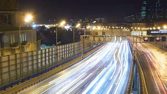 夜晚，河上桥上的车辆发出灯光。背景是摩天大楼。视频素材