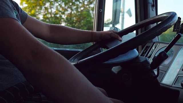 在炎热的夏天，一个面目全非的男人在乡村公路上驾驶着他的车，握着方向盘。卡车司机开车到达目的地。从卡车驾驶室看过去。慢镜头视频素材