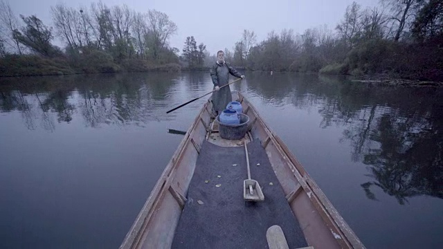 留着胡子的老渔夫穿着雨具，独自划着船沿着乡村的河流划下去视频下载
