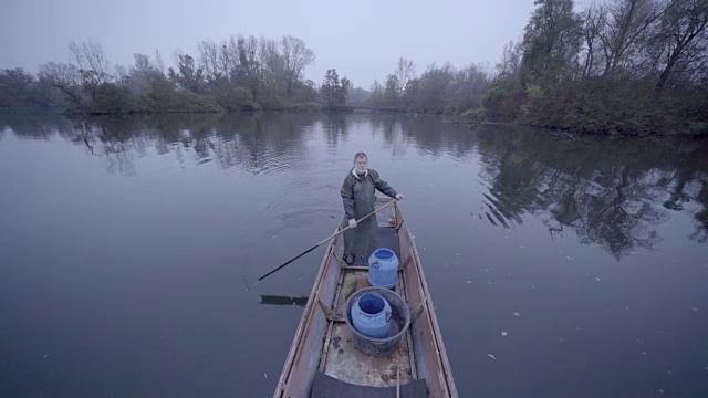 留着胡子的老渔夫穿着雨具，独自划着船沿着乡村的河流划下去视频素材