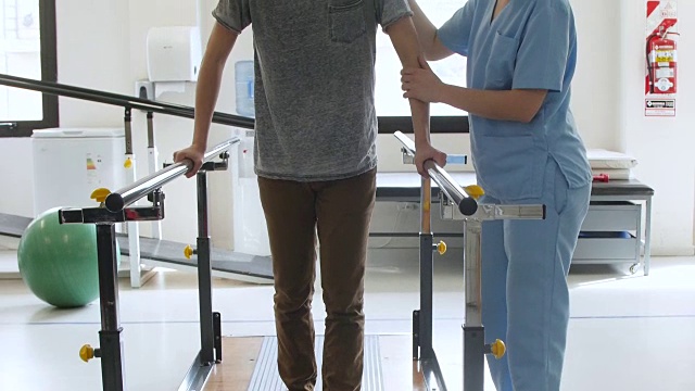 患者在双杠的帮助下微笑着行走，治疗师站在他旁边视频素材