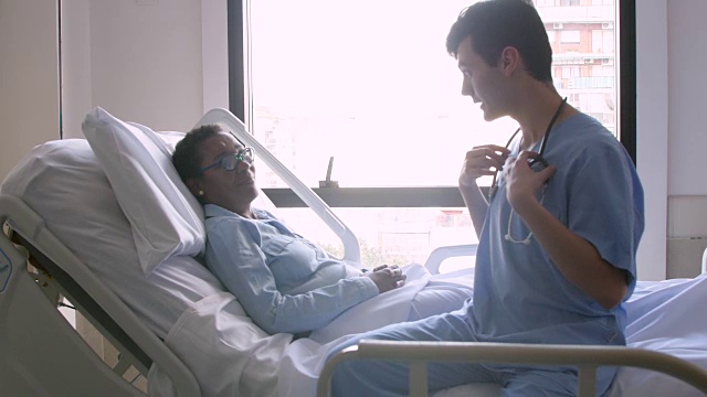 一位男性心脏病医生在病人躺在病床上时用听诊器对她说话视频下载