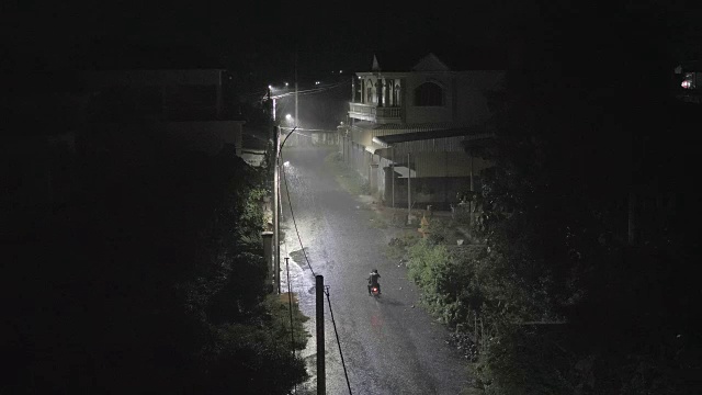 夜间有大雨。一个男人骑着摩托车在小街上视频素材