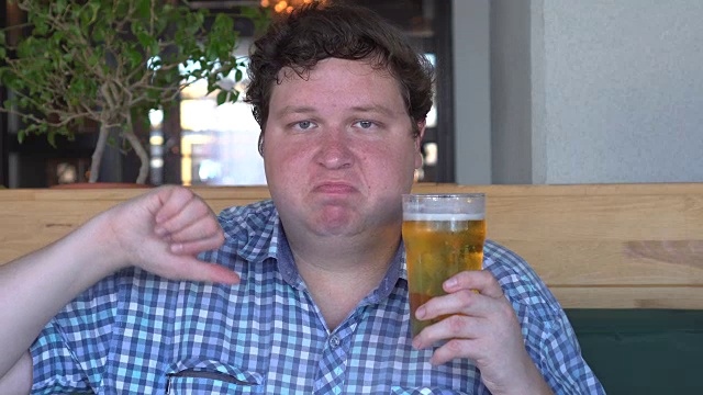 一个不满的年轻人拿着一杯啤酒，大拇指朝下视频下载