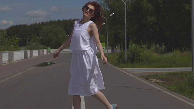 无忧无虑的年轻女孩在夏天的公园里蹦蹦跳跳。有魅力的女孩戴着墨镜，穿着白色的裙子在户外散步。慢动作视频下载