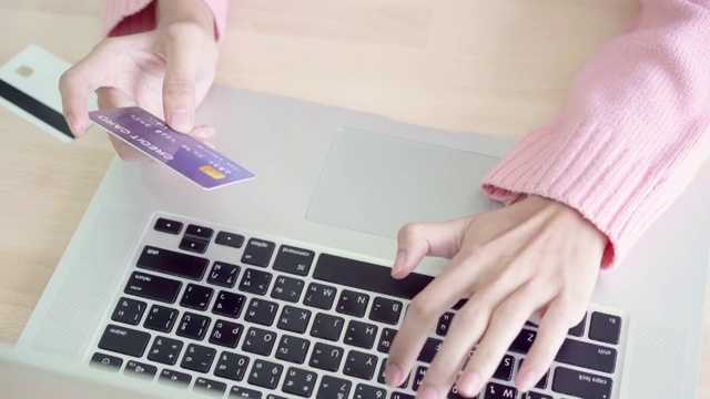 美丽的亚洲女人使用电脑或笔记本电脑购买网上购物的信用卡，而穿着毛衣坐在家里客厅的桌子上。生活方式女性在家的概念。视频素材