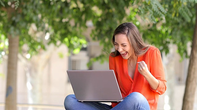 兴奋的女人在长凳上用笔记本电脑视频素材