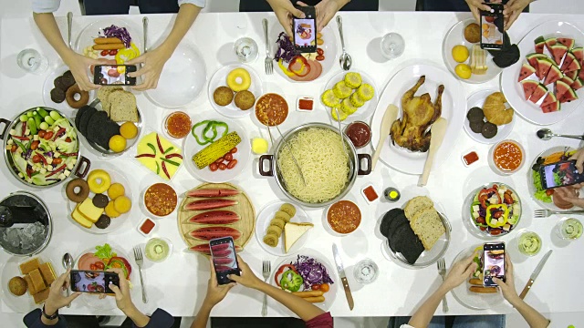 一群朋友在晚宴上所有人都在桌上用他们的智能手机拍晚餐食物的照片。Instagram，社交网络成瘾的概念。视频下载