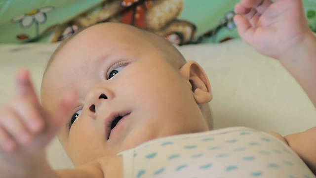 一个5个月大的婴儿躺在他孩子的床上的慢动作特写。视频下载
