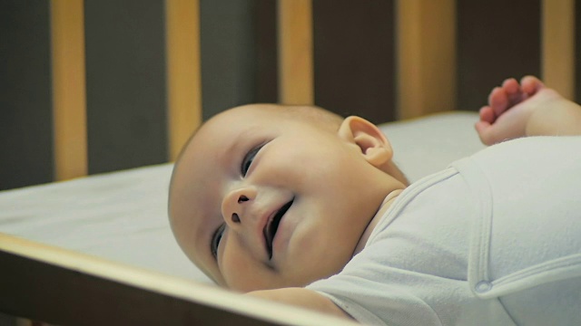 一个5个月大的婴儿微笑着躺在床上的慢动作特写。视频素材