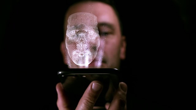 一名男性手持智能手机，屏幕上投射出他的3D脸部全息图视频下载
