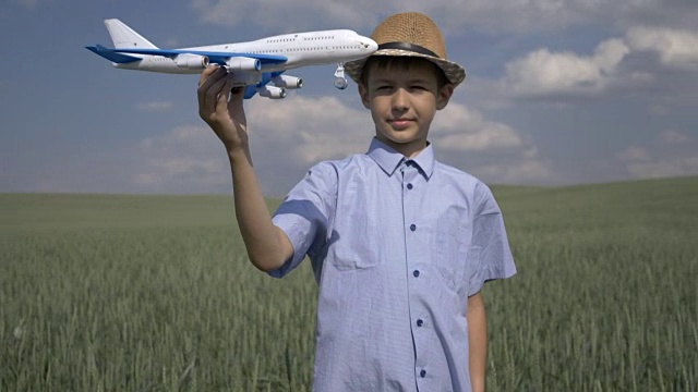 快乐的男孩梦想家手里拿着一架飞机，看着他，在户外视频下载