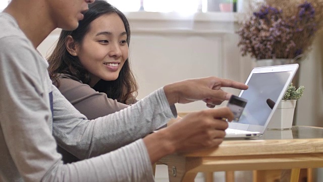 快乐的亚洲夫妇使用信用卡和笔记本电脑在家里进行网上购物视频素材
