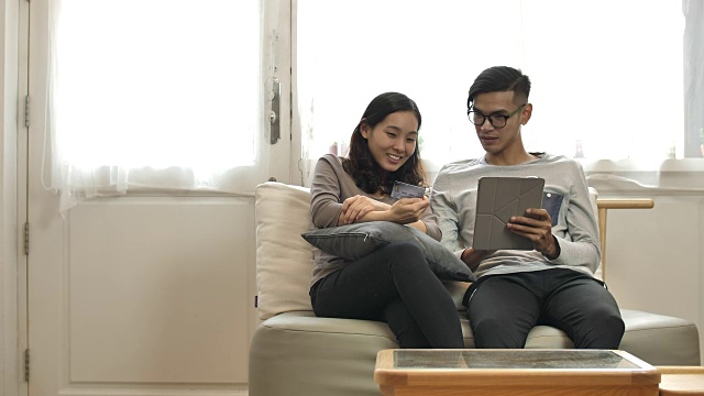 快乐的亚洲夫妇使用信用卡和数字平板电脑在家里在线购物视频素材