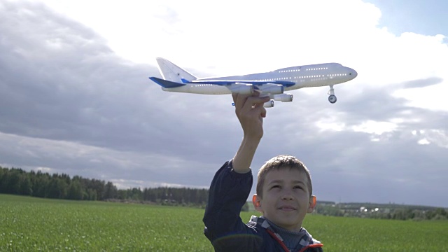 快乐的男孩梦想家手里拿着一架飞机，看着他，在户外视频素材