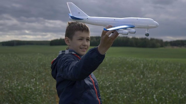 快乐的男孩梦想家手里拿着一架飞机，看着他，在户外视频素材