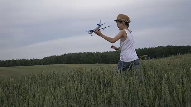 快乐的男孩梦想家戴着草帽跑过田野，手里拿着飞机，在户外视频素材