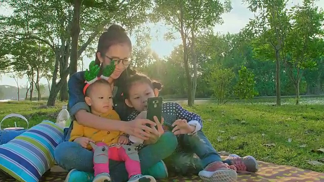 亚洲年轻母亲和女儿的孩子在户外用智能手机自拍视频素材