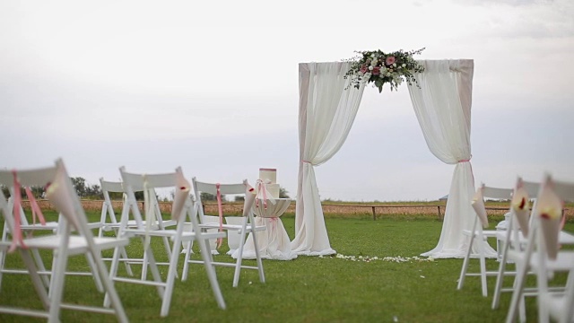 婚礼仪式。非常漂亮和时尚的婚礼拱门，装饰着各种鲜花和白布，站在绿色的草地上视频素材