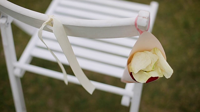 婚礼装饰:木椅上放婚礼装饰，白色椅子上放丝带和鲜花，小花瓶里放玫瑰花瓣和野花视频素材