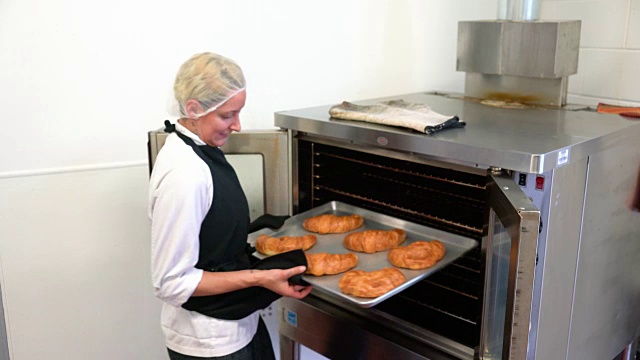 一位年轻的女面包师错误地用她的围裙端热烤盘。视频下载