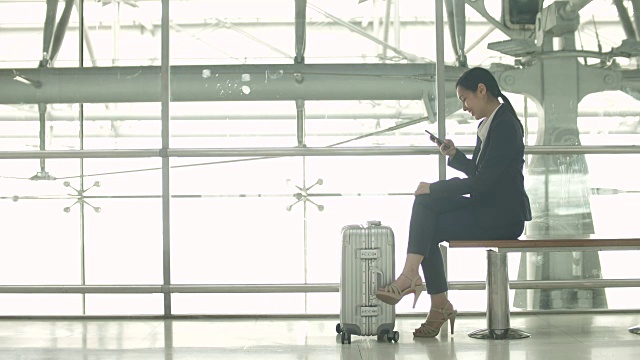 女商人在机场用智能手机坐在行李箱上视频素材