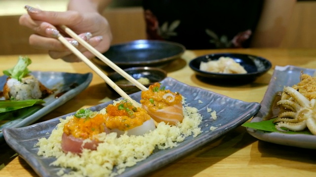 4K起重机拍摄:亚洲妇女喜欢用筷子吃生的三文鱼卷寿司。在舒士餐馆视频素材