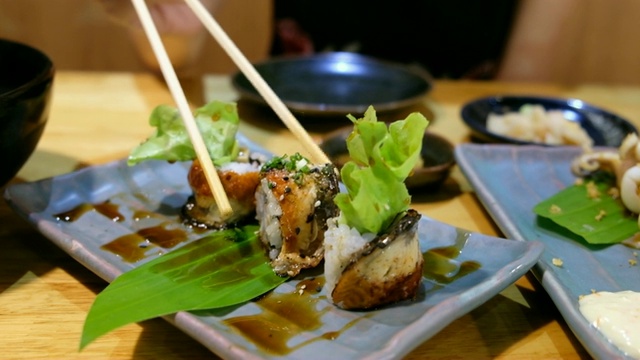 4K起重机拍摄:亚洲妇女喜欢用筷子吃鳗鱼寿司。在舒士餐馆视频素材