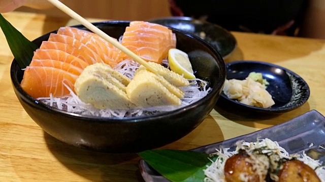 4K起重机拍摄:亚洲妇女喜欢用筷子吃冰的生鱼片鲑鱼。在日本餐厅视频素材