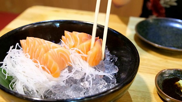 4K起重机拍摄:亚洲妇女喜欢用筷子吃冰的生鱼片鲑鱼。视频素材
