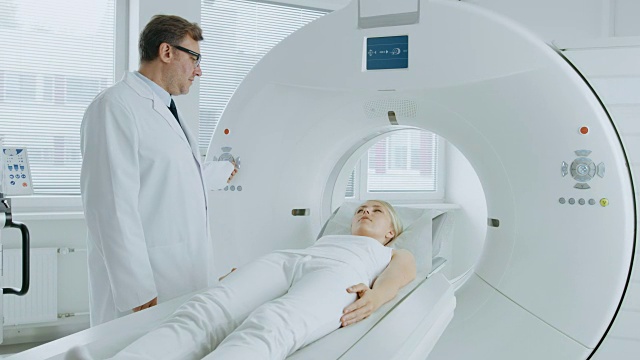 在医学实验室放射学家控制MRI或CT或PET扫描与女性病人正在进行的程序。专业医生运用先进的医疗技术进行紧急检查。视频素材