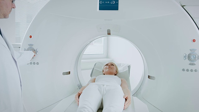 在医学实验室放射学家控制MRI或CT或PET扫描与女性病人正在进行的程序。高科技现代医疗设备。摄像头安装在床上，随病人移动。视频素材