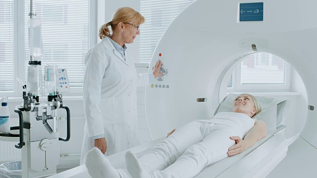 在医学实验室放射学家控制MRI或CT或PET扫描与女性病人正在进行的程序。高科技现代医疗设备。友好的医生与病人聊天。视频素材