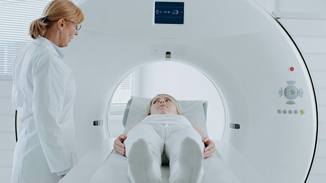 在医学实验室，女性病人躺在CT或MRI扫描床上，在专业放射学家的监督下进行扫描程序。病人在机器扫描时移动。视频素材
