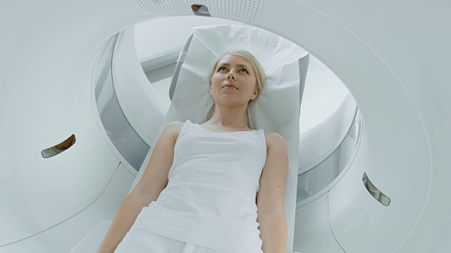 一个女性病人的特写肖像躺在一个CT或MRI扫描，床是移动机器扫描她的身体和大脑。在医疗实验室的高科技设备。提升相机拍摄。视频素材