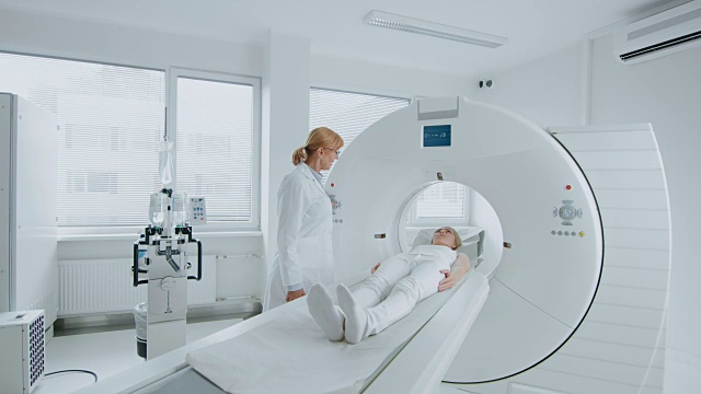 在医学实验室女性放射学家控制MRI或CT扫描与女性病人进行程序。高科技现代医疗设备。视频素材