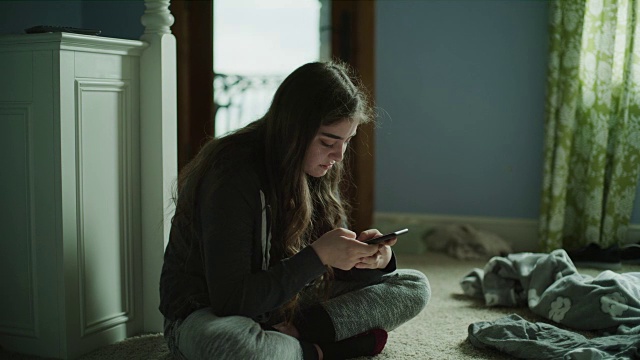 慢镜头拍摄的悲伤的女孩坐在地板上阅读手机/雪松山，犹他州，美国视频素材