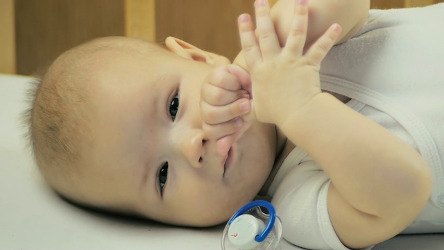 5个月大的婴儿一边看着镜头一边在床上吮吸手指。视频下载