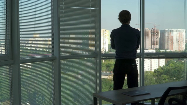 一个年轻人面对窗户站着，正在讲电话。视频下载
