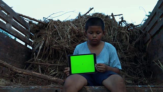 遭受自然灾害的亚洲男孩，拿着平板电脑的绿色屏幕，脸上带着悲伤。视频素材