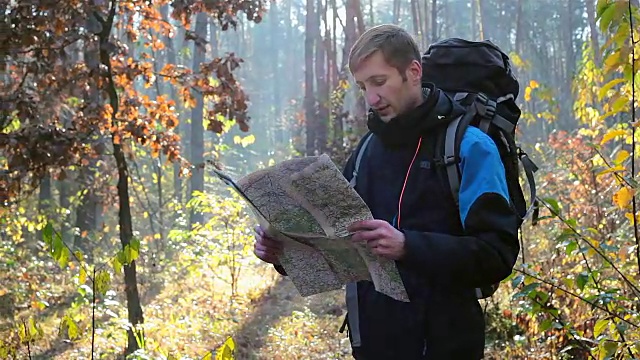 一个旅行者手里拿着一张地图走在一个陌生的森林里。视频下载