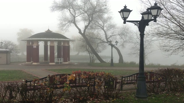 漫步在公园的步行街，沉浸在浓浓的雾中。可见旧式的灯笼和长凳。视频素材