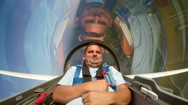 一个年轻人在阳光灿烂的天空中，坐在滑翔机的后面大笑视频下载
