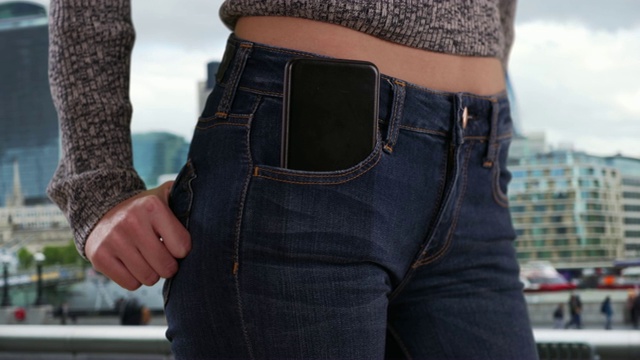 特写的年轻女士的腰部与手机在口袋与城市景观的背景视频素材