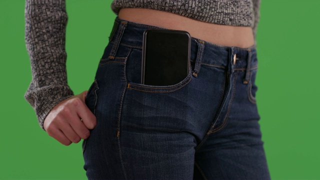 近距离的女人在绿色屏幕上的蓝色牛仔裤与手机在前面的口袋视频素材