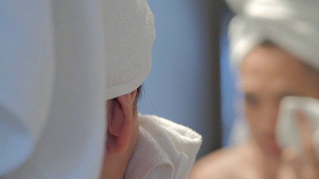 快乐的年轻女子，皮肤干净，用白色的毛巾在她的头上洗脸。年轻女子在浴室里用毛巾擦脸。痤疮视频素材