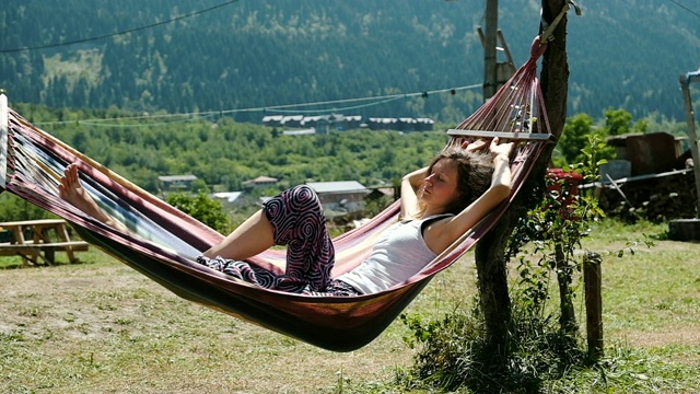 女孩睡在一张吊床上，大自然的背景是青山，慢镜头视频下载